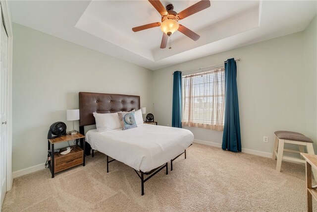 carpeted bedroom with ceiling fan, a tray ceiling, and a closet