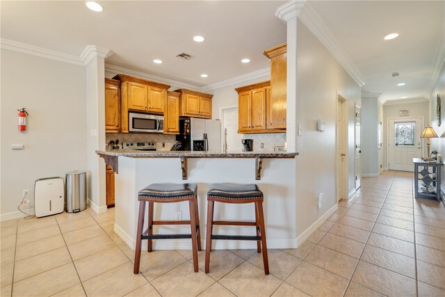 kitchen with appliances with stainless steel finishes, decorative backsplash, light stone counters, and ornamental molding