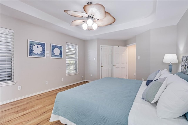 bedroom with light wood-type flooring, a raised ceiling, and ceiling fan