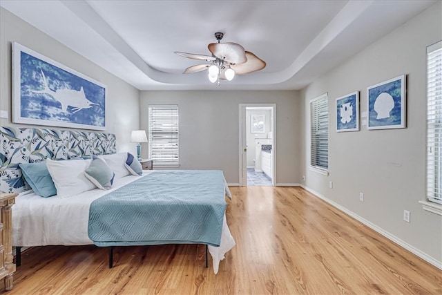 bedroom with a tray ceiling, ensuite bath, ceiling fan, and light hardwood / wood-style flooring