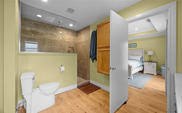 bathroom featuring toilet, hardwood / wood-style flooring, a tile shower, and crown molding