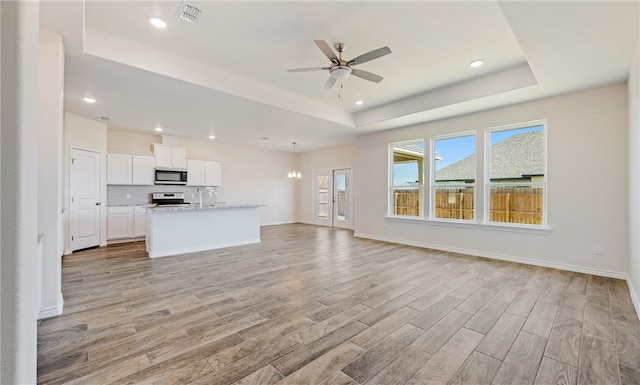 unfurnished living room featuring visible vents, a raised ceiling, light wood-style flooring, and ceiling fan with notable chandelier