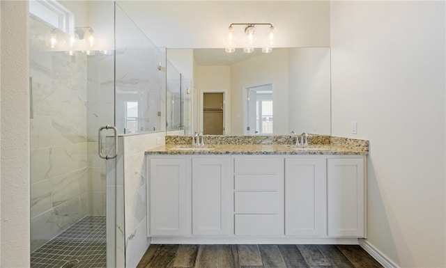 full bathroom with a stall shower, a sink, wood finished floors, double vanity, and a spacious closet