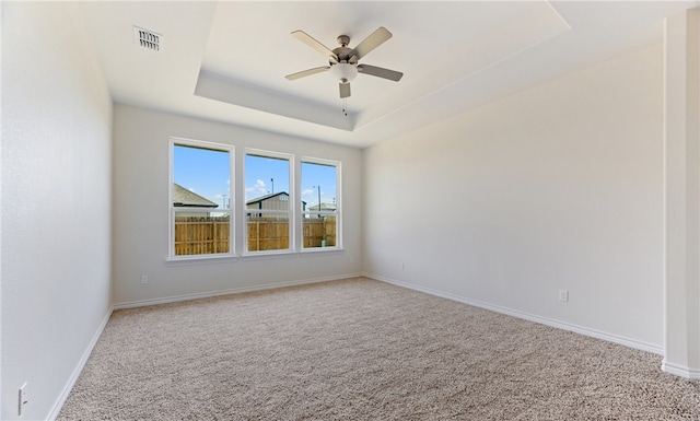 carpeted spare room with a ceiling fan, a tray ceiling, baseboards, and visible vents