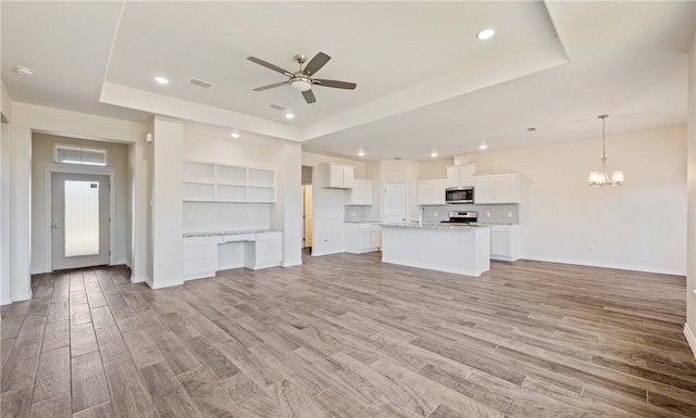 unfurnished living room featuring a raised ceiling, ceiling fan with notable chandelier, baseboards, and light wood finished floors