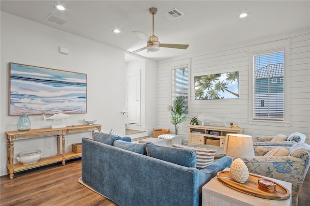 living room with wood walls, plenty of natural light, wood-type flooring, and ceiling fan