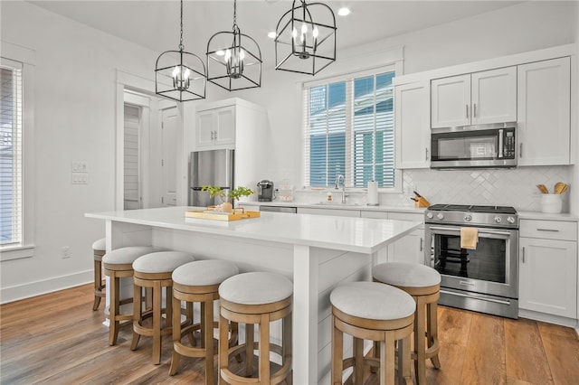 kitchen featuring light wood-type flooring, appliances with stainless steel finishes, decorative light fixtures, white cabinets, and a center island