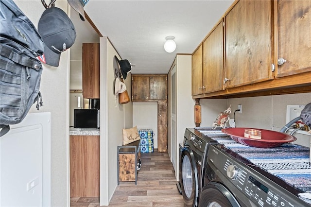 clothes washing area with cabinets, washer and clothes dryer, and light hardwood / wood-style floors