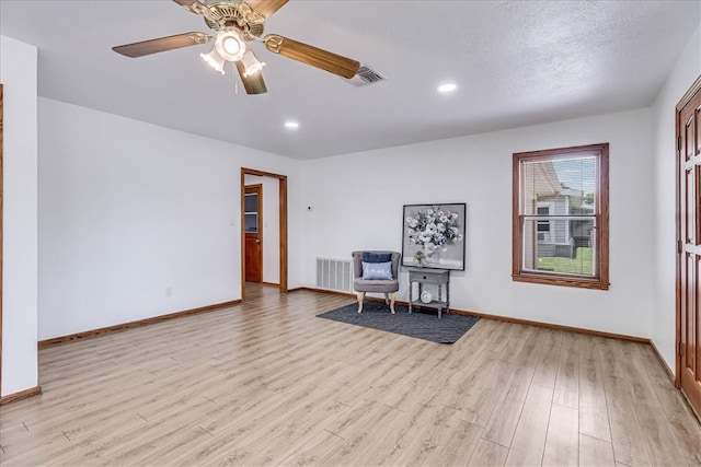 living area featuring a textured ceiling, light hardwood / wood-style floors, and ceiling fan