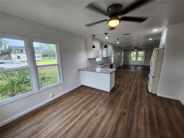 kitchen with white cabinetry, light stone countertops, white refrigerator, backsplash, and kitchen peninsula