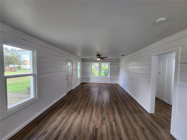 unfurnished living room with ceiling fan, wooden walls, and dark wood-type flooring