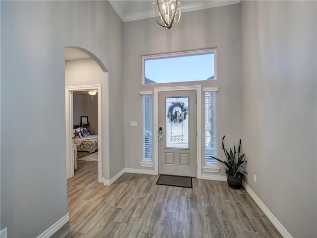 foyer featuring wood finished floors, arched walkways, a high ceiling, crown molding, and baseboards