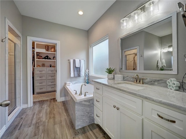 full bath with a walk in closet, a bath, wood finished floors, and a stall shower