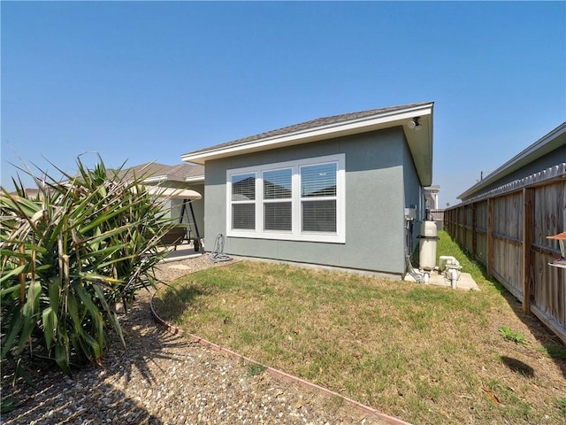 back of property featuring stucco siding, a yard, and fence