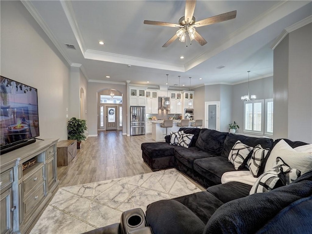 living area with a tray ceiling, arched walkways, visible vents, and ceiling fan with notable chandelier