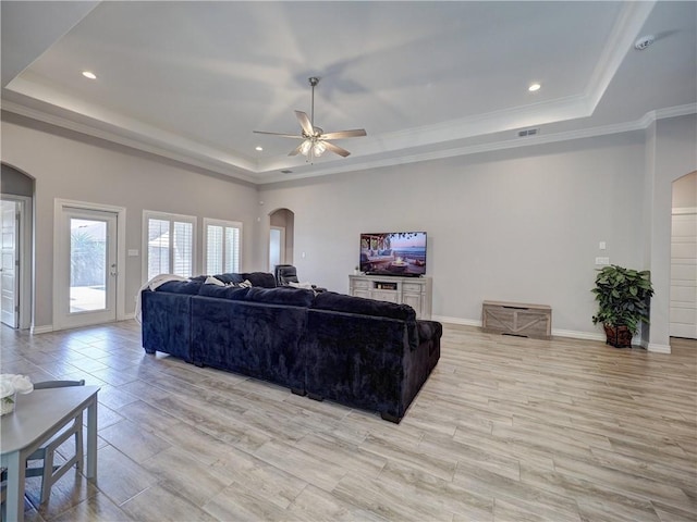 living room featuring a tray ceiling, baseboards, arched walkways, and ceiling fan