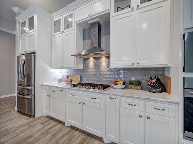 kitchen featuring decorative backsplash, white cabinets, stainless steel appliances, and wall chimney range hood