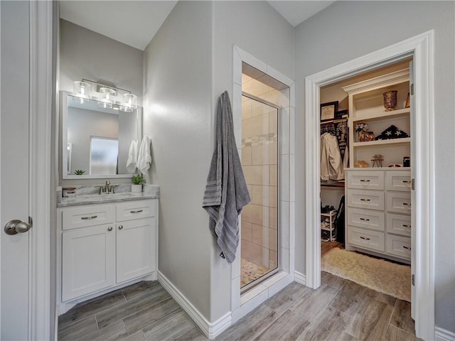 full bathroom with wood finish floors, a spacious closet, and a shower stall