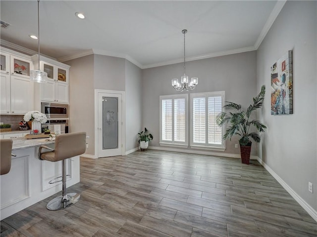 kitchen with glass insert cabinets, stainless steel appliances, an inviting chandelier, wood finished floors, and white cabinetry