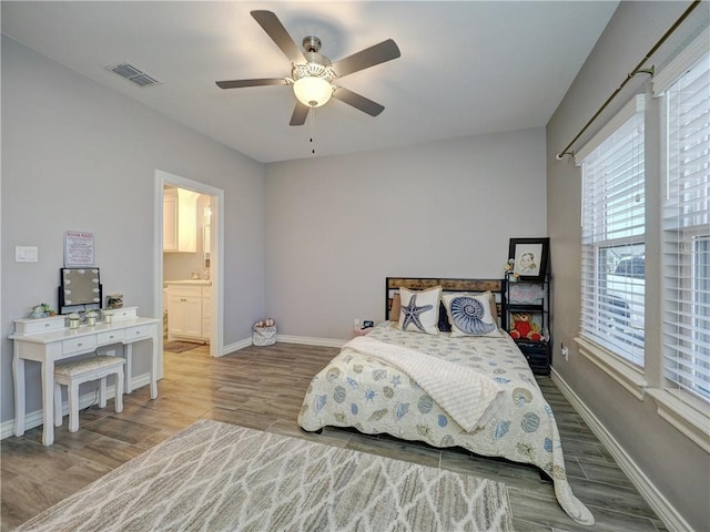 bedroom with visible vents, ensuite bathroom, wood finished floors, baseboards, and ceiling fan