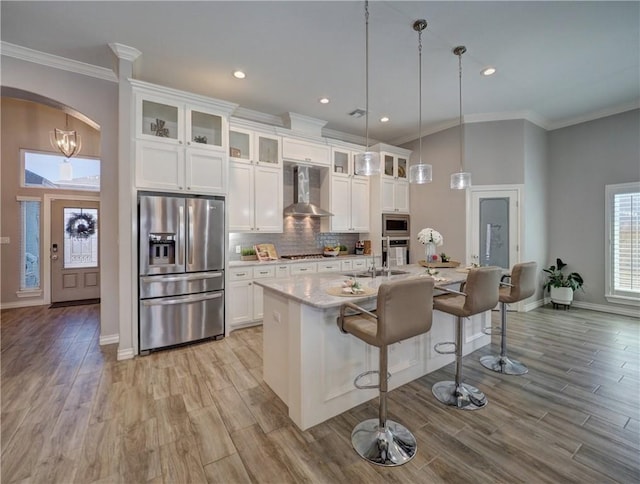 kitchen with backsplash, wall chimney range hood, ornamental molding, stainless steel appliances, and white cabinetry