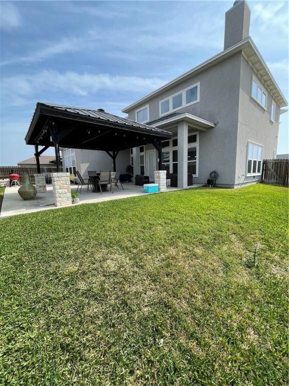 rear view of property featuring fence, a chimney, stucco siding, a patio area, and a lawn