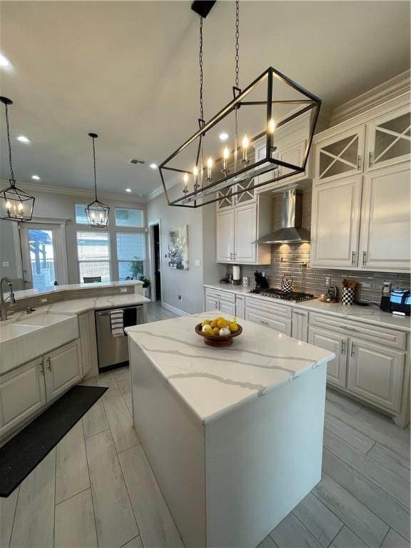 kitchen featuring a kitchen island, a chandelier, stainless steel appliances, wall chimney exhaust hood, and a sink