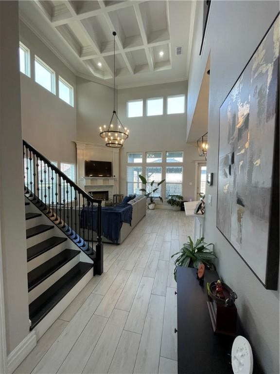 interior space with stairway, coffered ceiling, wood tiled floor, an inviting chandelier, and a fireplace