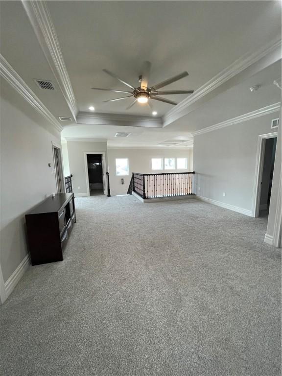 unfurnished living room featuring a ceiling fan, a tray ceiling, carpet flooring, crown molding, and baseboards