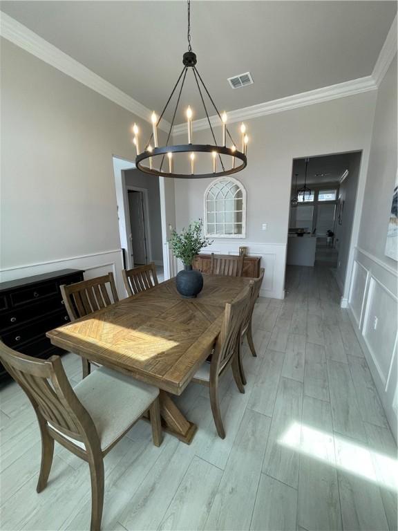 dining space featuring visible vents, light wood-style floors, crown molding, a decorative wall, and a notable chandelier