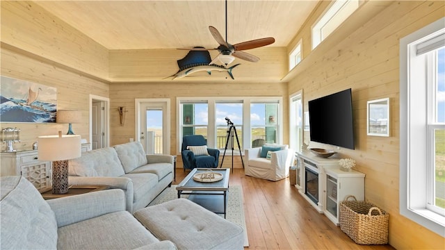 living room featuring wooden walls, light hardwood / wood-style flooring, high vaulted ceiling, and a healthy amount of sunlight