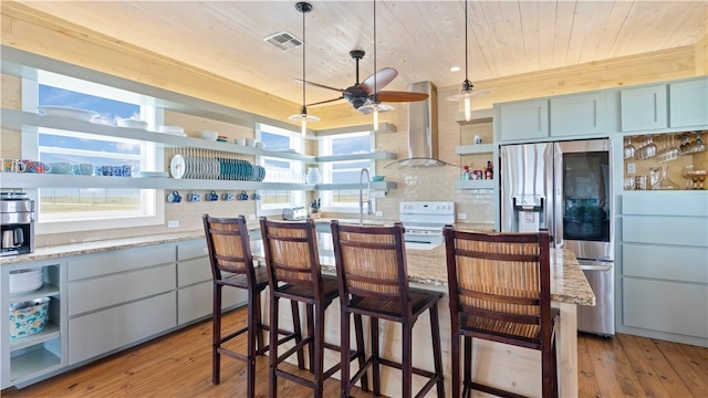 kitchen with stainless steel fridge, light wood-type flooring, wall chimney range hood, and white stove