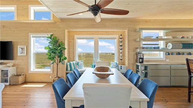 dining space with hardwood / wood-style flooring, a wealth of natural light, wooden walls, and ceiling fan