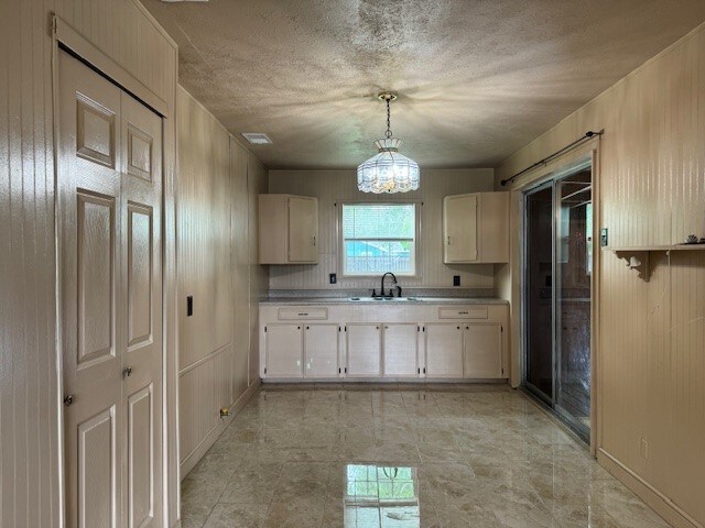 kitchen with a notable chandelier, a textured ceiling, sink, wood walls, and pendant lighting