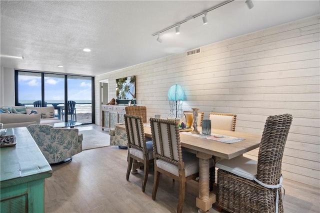 dining area featuring a textured ceiling, wood finished floors, visible vents, a wall of windows, and track lighting