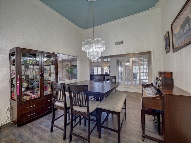 dining space featuring a high ceiling, wood-type flooring, crown molding, and an inviting chandelier