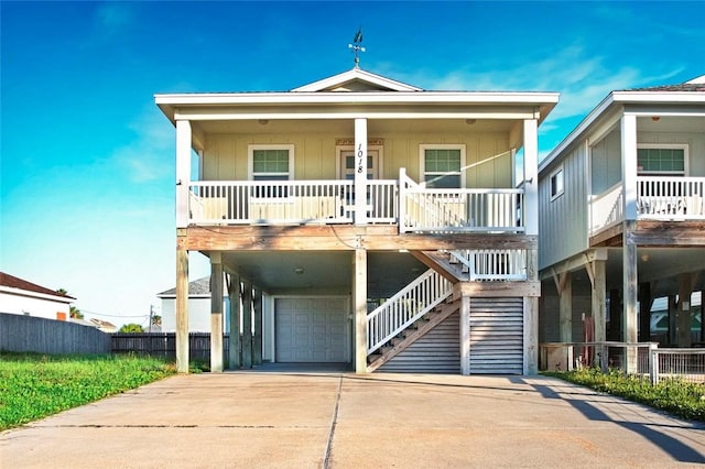 beach home with a garage, covered porch, concrete driveway, fence, and stairs