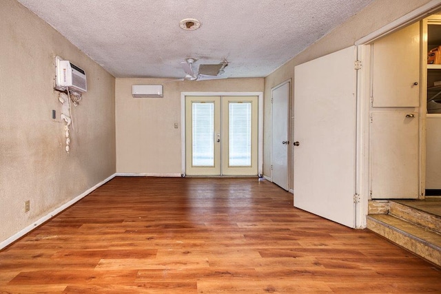 interior space featuring french doors, light wood-type flooring, a textured ceiling, and a wall mounted air conditioner