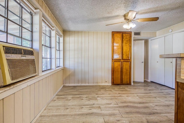 spare room with cooling unit, wood walls, a textured ceiling, ceiling fan, and light hardwood / wood-style flooring