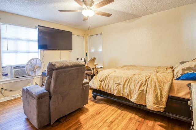 bedroom with a textured ceiling, light hardwood / wood-style flooring, cooling unit, and ceiling fan