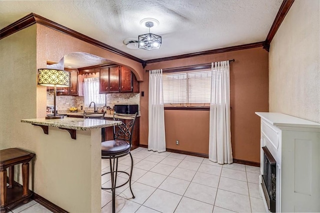 kitchen featuring decorative light fixtures, a kitchen breakfast bar, decorative backsplash, light stone counters, and crown molding