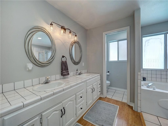 full bath with double vanity, toilet, a sink, and wood finished floors