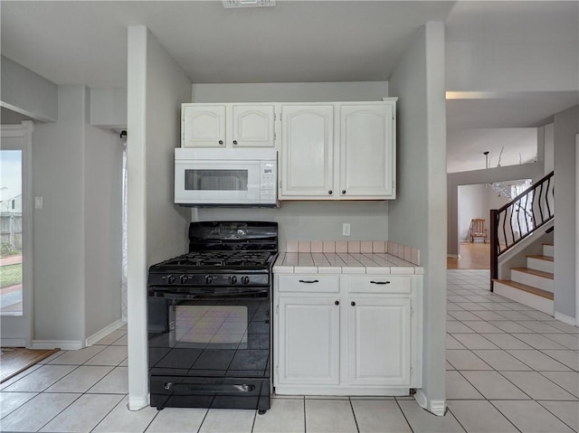 kitchen featuring light tile patterned flooring, white microwave, tile counters, white cabinets, and black range with gas cooktop