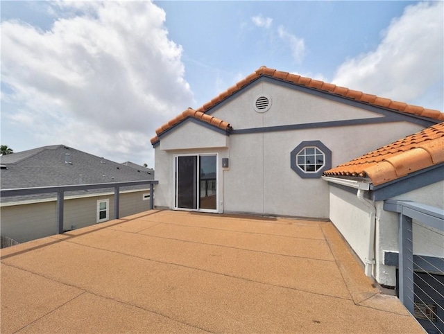 rear view of property featuring a patio, stucco siding, and a tiled roof