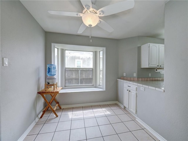 kitchen featuring white cabinets, tile counters, a ceiling fan, baseboards, and light tile patterned floors
