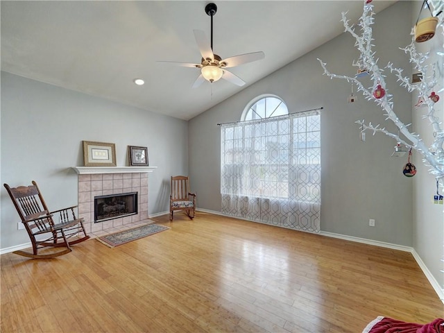 unfurnished room with a tiled fireplace, lofted ceiling, wood finished floors, and ceiling fan