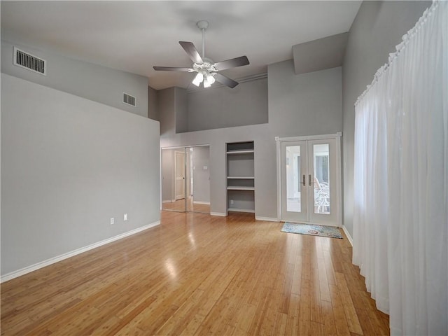 unfurnished living room with light wood-style floors, french doors, a ceiling fan, a towering ceiling, and visible vents