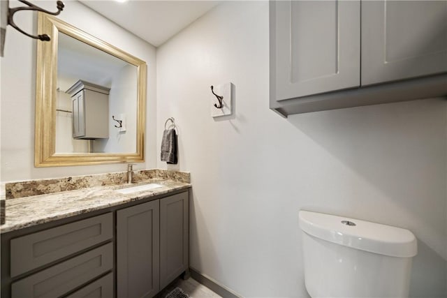 half bath with baseboards, vanity, and toilet