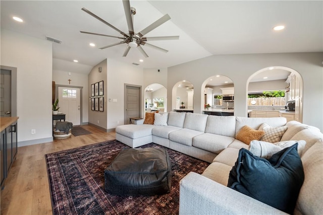 living room with arched walkways, light wood-type flooring, vaulted ceiling, visible vents, and a ceiling fan