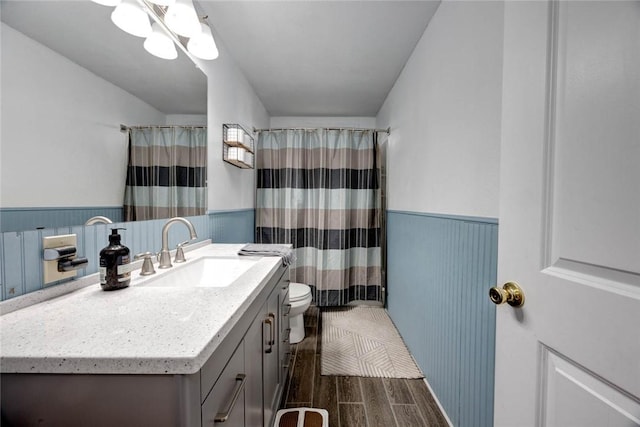 full bath with a wainscoted wall, a shower with shower curtain, toilet, wood tiled floor, and vanity